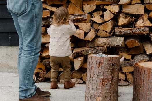 Back view of unrecognizable child and father standing near firewood in backyard and enjoying weekend while spending time together in countryside